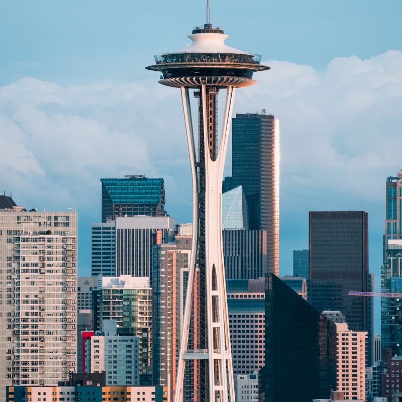 The image shows the Space Needle in Seattle, surrounded by skyscrapers, under a partly cloudy sky.