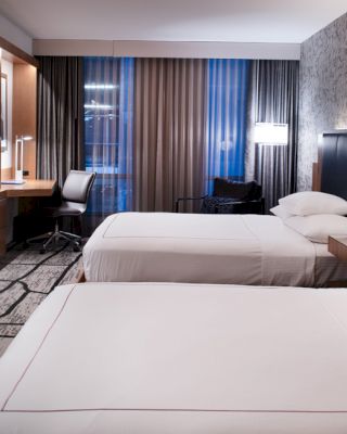 A modern hotel room with two beds, a flat-screen TV, a desk, lamps, and a patterned wall.