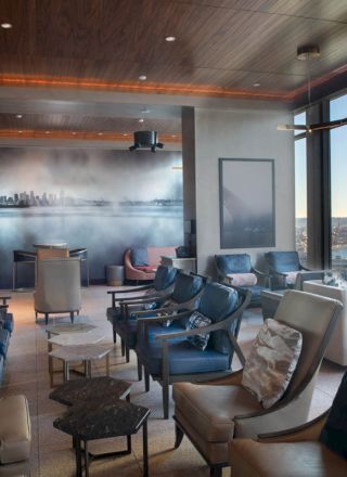 A modern lounge with comfortable seating, large windows offering a scenic view, and stylish decor featuring a cityscape mural on the wall.