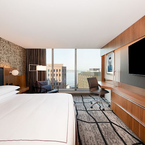 A modern hotel room with a large bed, TV, desk, and window view. Wood accents and a patterned wall add to the contemporary design.